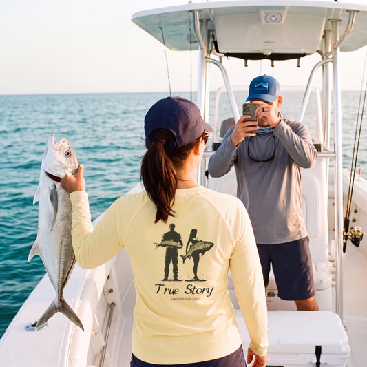 True Story women's performance shirt in yellow, holding up the catch while her partner takes the photo