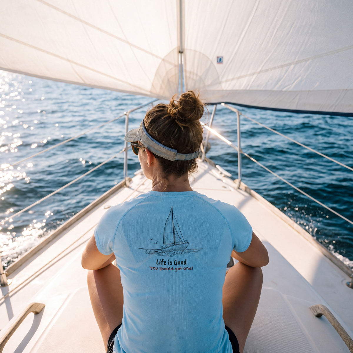 Woman on the bow of a sailboat in the light blue Life Is Good women's performance tee