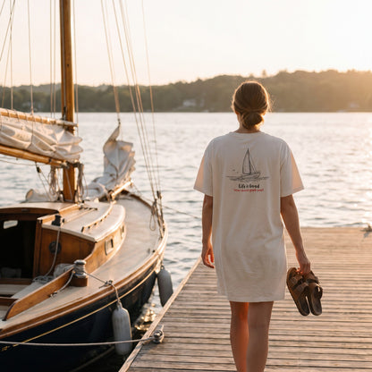Life Is Good dress tee walking down a sailboat dock at sunset, sandals in hand