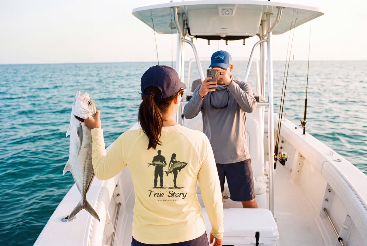 Angler on a center-console boat holding up her catch in the yellow True Story women's performance shirt from Mariner's Threads while her partner snaps the photo